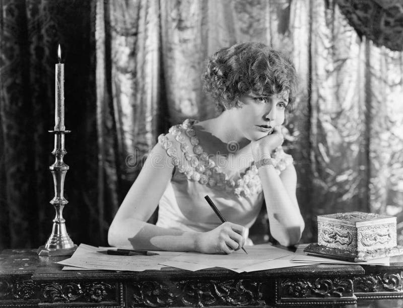 Jeune femme s'asseyant à un bureau avec un stylo à disposition, regardant triste tout en écrivant une lettre (toutes les personne images libres de droits