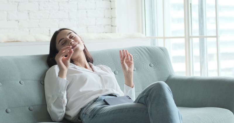 Jeune femme se relaxer sur un canapé confortable en écoutant de la musique lounge en direct via l'application smartphone clips vidéos