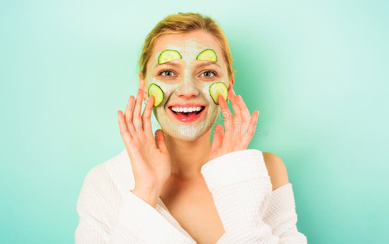 Jeune femme souriante avec masque cosmétique en argile et tranches de concombre frais sur le visage dans le salon de spa. Masque f photographie stock libre de droits
