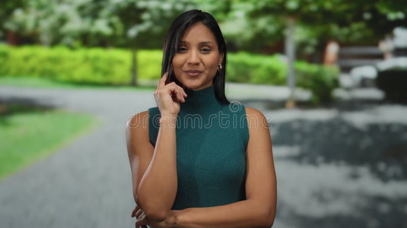 Jeune femme souriante debout dans un parc verdoyant à l'extérieur exsument la confiance avec sa pose mannequin et sa tenue décontr clips vidéos