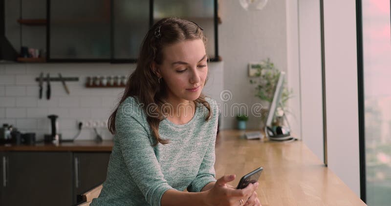Jeune femme souriante détendue utilisant smartphone dans la cuisine moderne. banque de vidéos