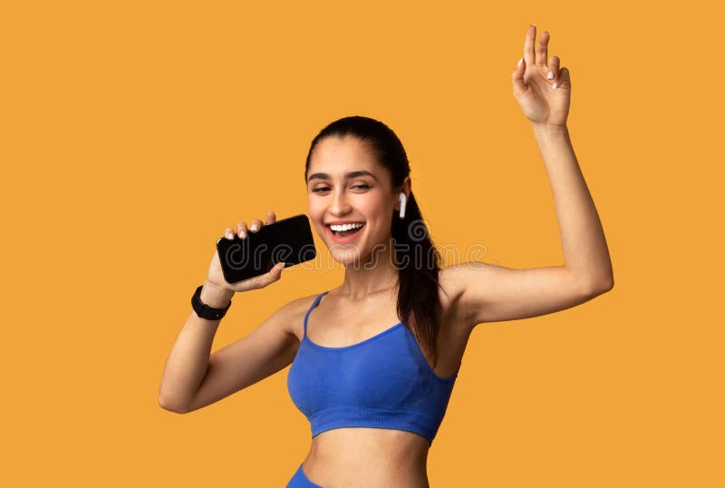 Jeune femme souriante en sportswear chantant tenant un téléphone portable images libres de droits