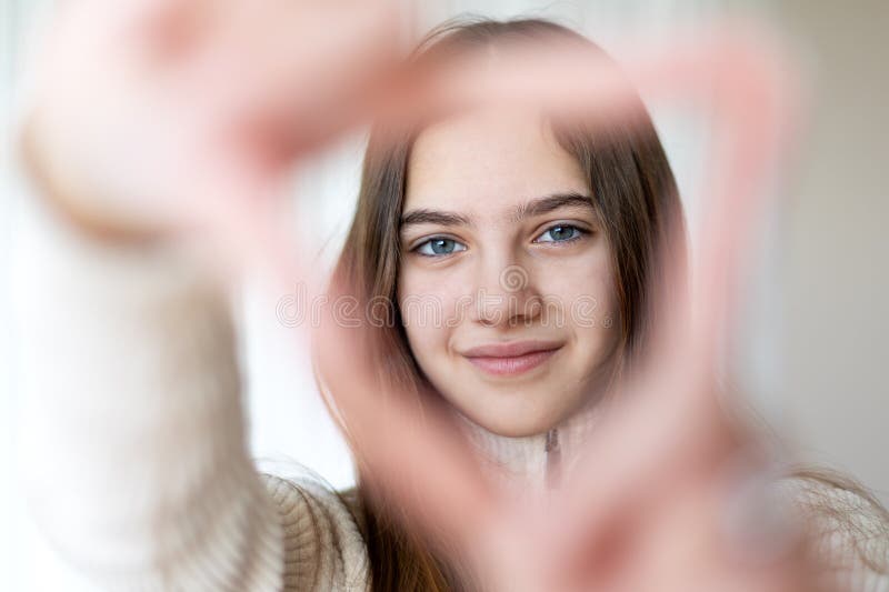 Jeune femme souriante encadrée par un geste de coeur. portrait d'une jeune femme souriant doucement avec ses mains formant un coeu photographie stock libre de droits