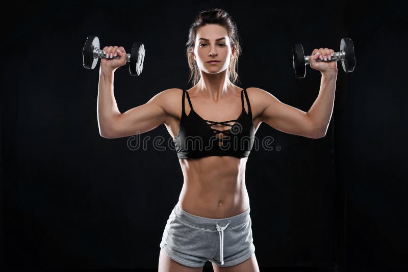 Jeune femme sportive faisant une séance d'exercice de remise en forme avec des haltères sur le fond noir de studio images stock