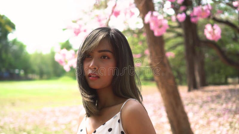 Jeune femme superbe pensant et regardant loin dans le parc. Position occupée absente de fille mignonne dans le jardin fleuri. banque de vidéos
