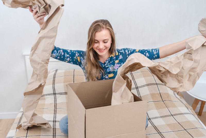 Jeune femme surprise assise sur son lit déballage boîte en carton à la maison. livraison de colis photographie stock libre de droits