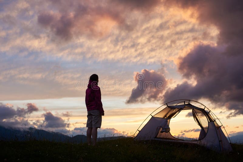 Jeune femme tenant le camp proche, beau coucher du soleil de nature sur la montagne image stock Jeune femme tenant le camp proche, beau coucher du soleil de nature sur la montagne image stock