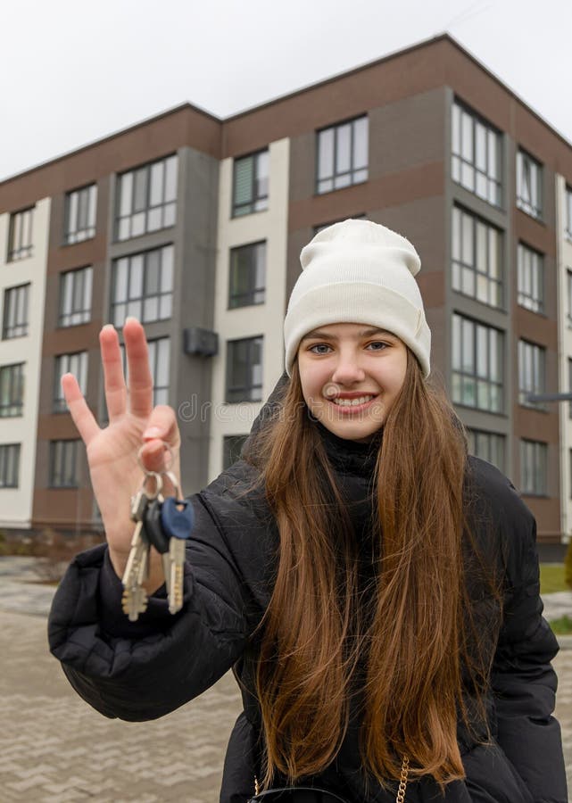 Jeune femme tenant les clés du nouvel appartement. jeune femme souriante dans un beanie blanche tenant les clés debout devant un image stock