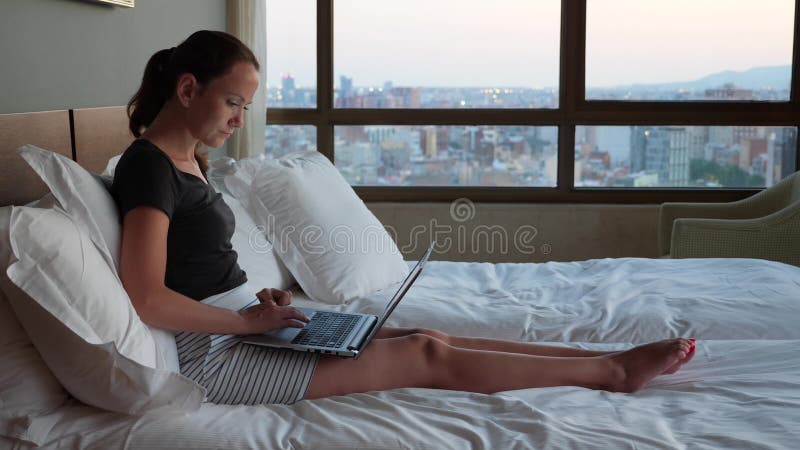 Jeune femme travaillant sur l'ordinateur portable dans le lit