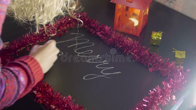 Jeune femme écrivant le texte de Joyeux Noël sur un tableau sur la table noire banque de vidéos