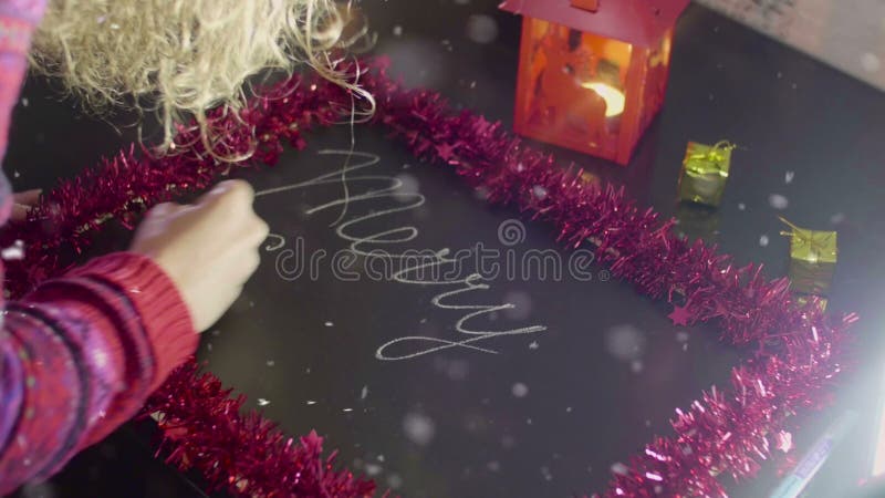 Jeune femme écrivant le texte de Joyeux Noël sur un tableau sur la table noire banque de vidéos