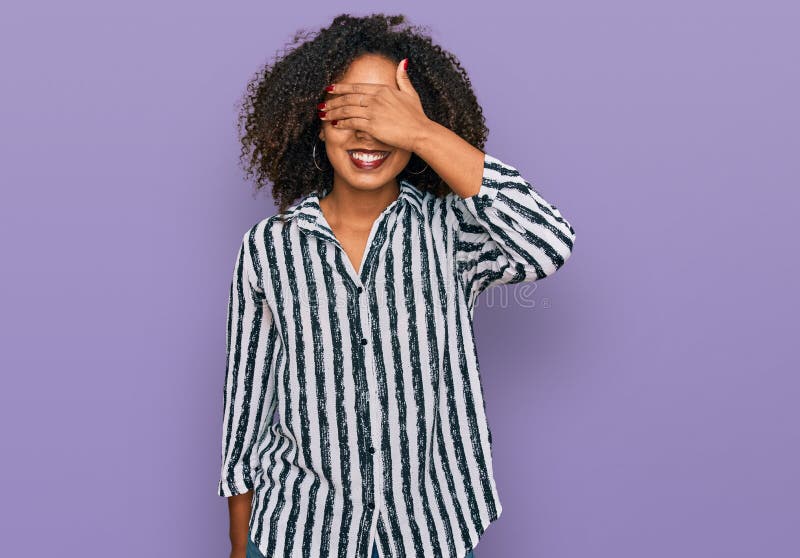 Jeune fille afro-américaine portant des vêtements décontractés souriant et riant de main en main en couvrant les yeux pour la surp photos libres de droits