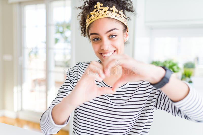 Jeune fille afro-américaine portant la couronne de reine d'or sur la tête souriant amoureux montrant symbole du coeur et forme ave photos stock