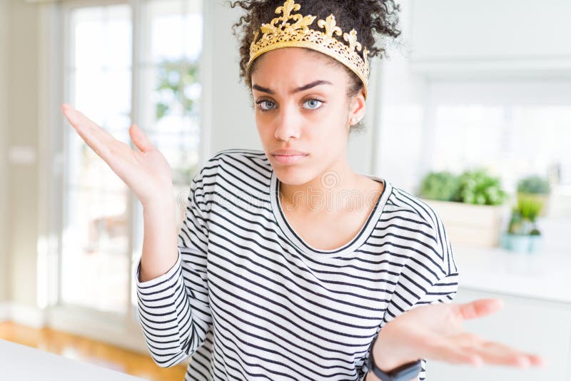 Jeune fille afro-américaine portant la couronne de reine d'or sur la tête une expression déroutante et confuse avec les bras et le photos libres de droits