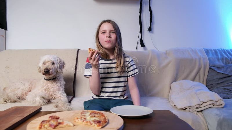 Jeune fille aime pizza avec chien de compagnie sur un canapé confortable dans le salon lumineux banque de vidéos