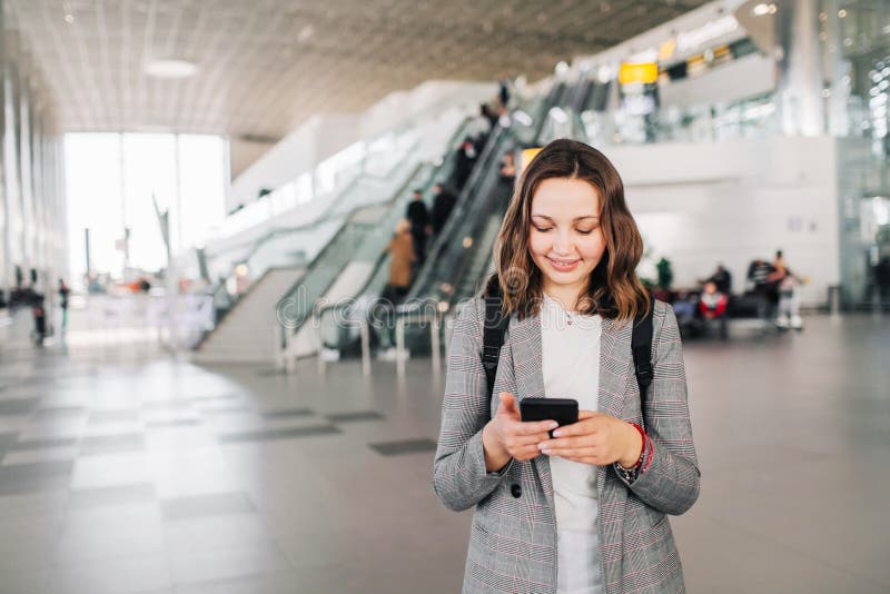 Jeune fille aux promenades d'aéroport avec son sourire de smartphone photographie stock Jeune fille aux promenades d'aéroport avec son sourire de smartphone photographie stock