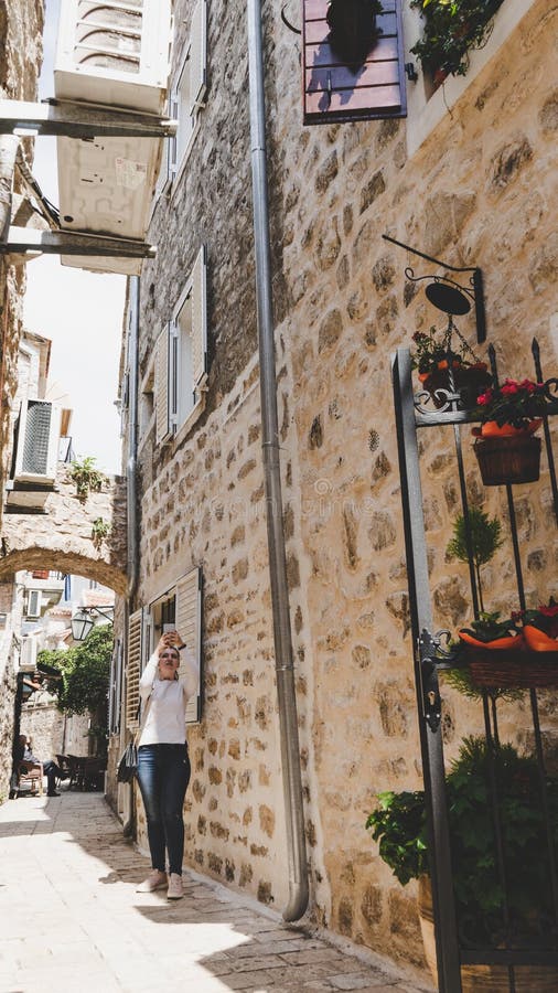 Jeune fille blanche prenant des photos dans les petites rues étroites de la vieille ville de Budva, Monténégro Femme marchant ent photographie stock Jeune fille blanche prenant des photos dans les petites rues étroites de la vieille ville de Budva, Monténégro Femme marchant ent photographie stock