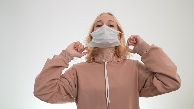 Jeune fille blonde enlève le masque de coronavirus sur un fond léger.