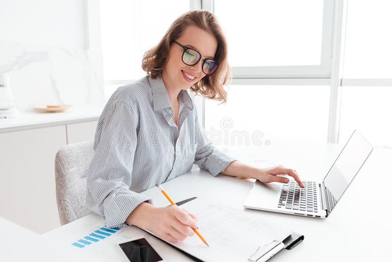 Jeune fille de sourire attirante dans les verres et le worki de chemise rayée photographie stock Jeune fille de sourire attirante dans les verres et le worki de chemise rayée photographie stock
