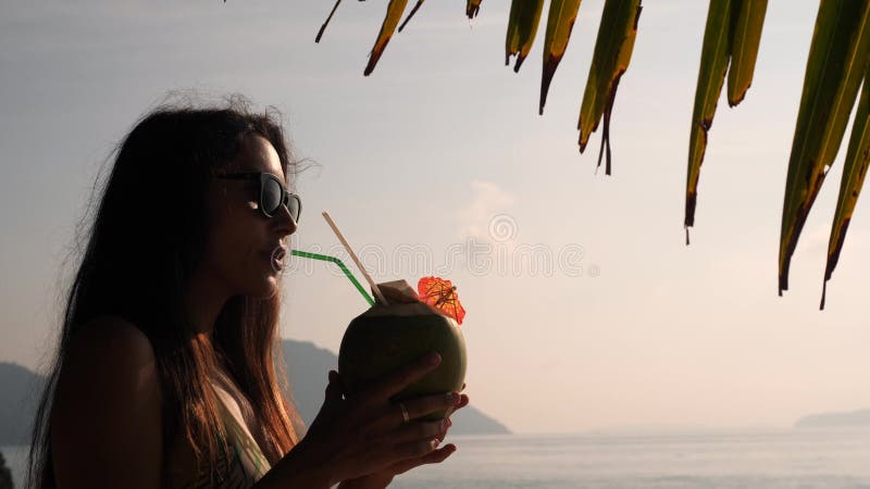 Jeune fille de touristes Enjoing buvant le cocktail thaïlandais frais de l'eau de noix de coco à la plage tropicale 4K, au ralent banque de vidéos