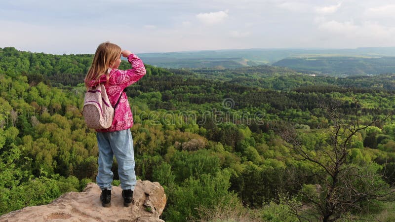 Jeune fille debout sur une falaise rocheuse regardant un paysage forestier panoramique clips vidéos