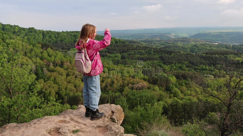 Jeune fille debout sur une falaise rocheuse regardant un paysage forestier panoramique banque de vidéos