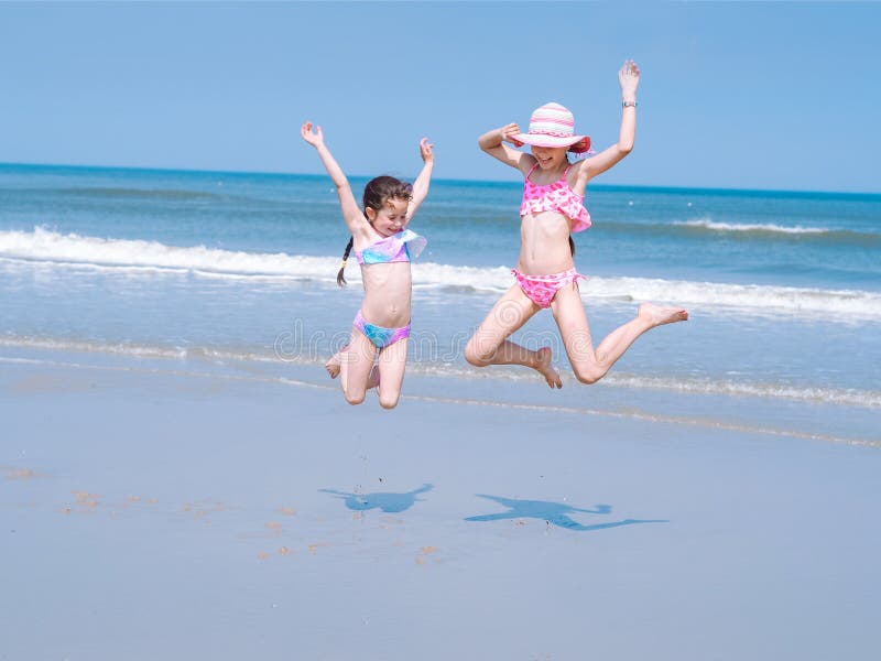 Jeune fille deux heureuse ayant l'amusement sur la plage tropicale et sautant dans le maillot de bain dans l'air sur la côte au t photographie stock Jeune fille deux heureuse ayant l'amusement sur la plage tropicale et sautant dans le maillot de bain dans l'air sur la côte au t photographie stock