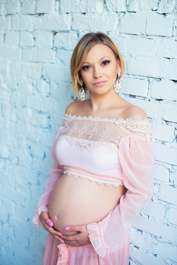 Jeune fille enceinte avec du charme près d'un mur de briques blanc étreignant le ventre photos libres de droits Jeune fille enceinte avec du charme près d'un mur de briques blanc étreignant le ventre photos libres de droits
