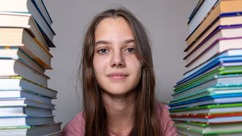 Jeune fille entourée de piles de livres. une adolescente confiante assise entre de grandes piles de livres colorés images stock