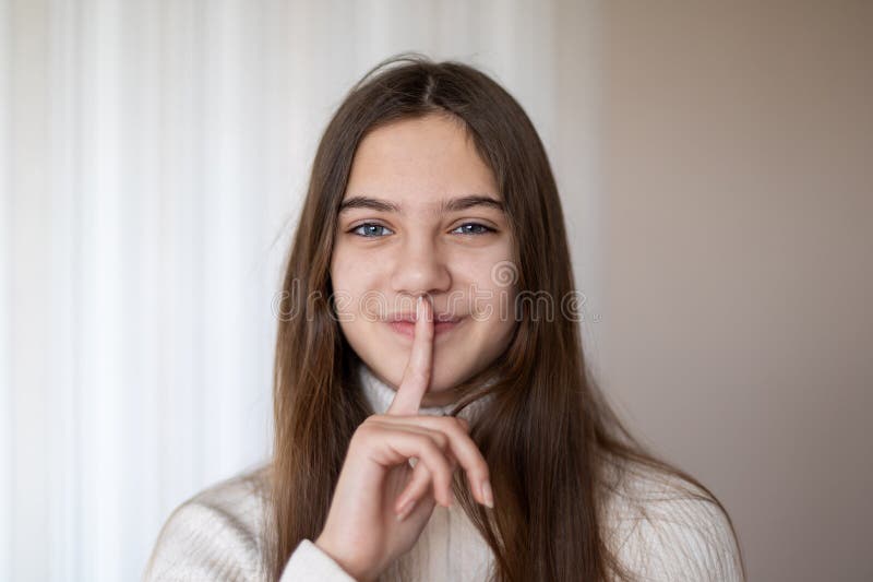 Jeune fille gestant pour le silence avec le doigt. portrait d'une jeune femme aux cheveux longs souriant joyeusement tout en tenan photo libre de droits