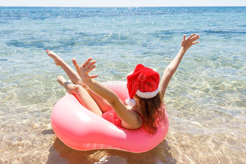 Jeune fille heureuse avec le chapeau de Santa Claus dans un flotteur arrosé de beignet en mer, souriant avec des lunettes de sole image libre de droits Jeune fille heureuse avec le chapeau de Santa Claus dans un flotteur arrosé de beignet en mer, souriant avec des lunettes de sole image libre de droits