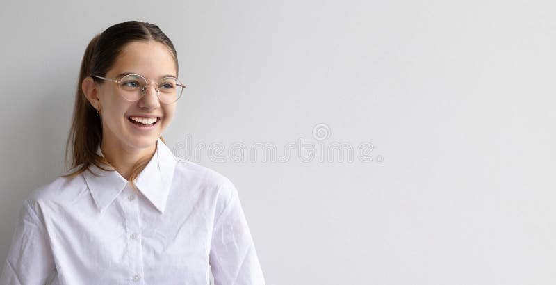 Jeune fille heureuse portant des lunettes souriant sur fond blanc. une jeune fille avec des lunettes et une queue de cheval sourit. une jeune fille avec des lunettes et une queue de cheval est souriante tout en se tenant sur un fond blanc clair.
