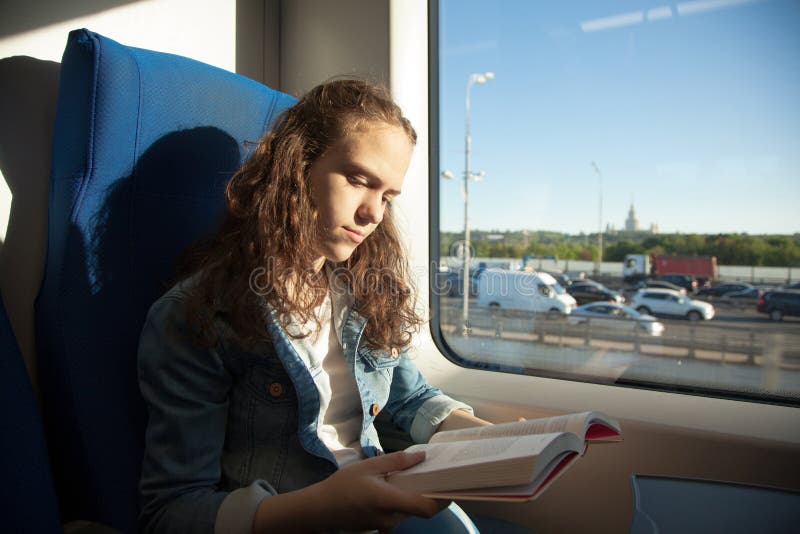 Jeune fille lisant un livre tandis que sur un train à une lumière du soleil photo stock Jeune fille lisant un livre tandis que sur un train à une lumière du soleil photo stock