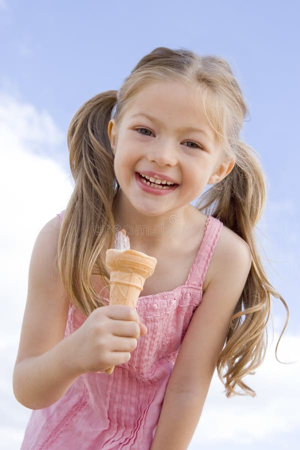 Jeune fille mangeant à l'extérieur le cône de crême glacée photo stock