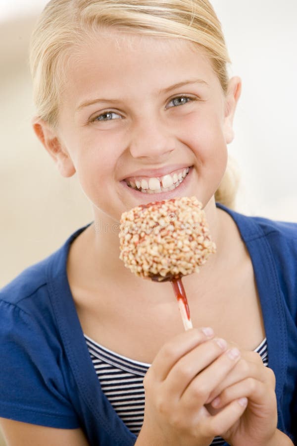Jeune fille mangeant à l'intérieur la pomme de sucrerie photo stock Jeune fille mangeant à l'intérieur la pomme de sucrerie photo stock