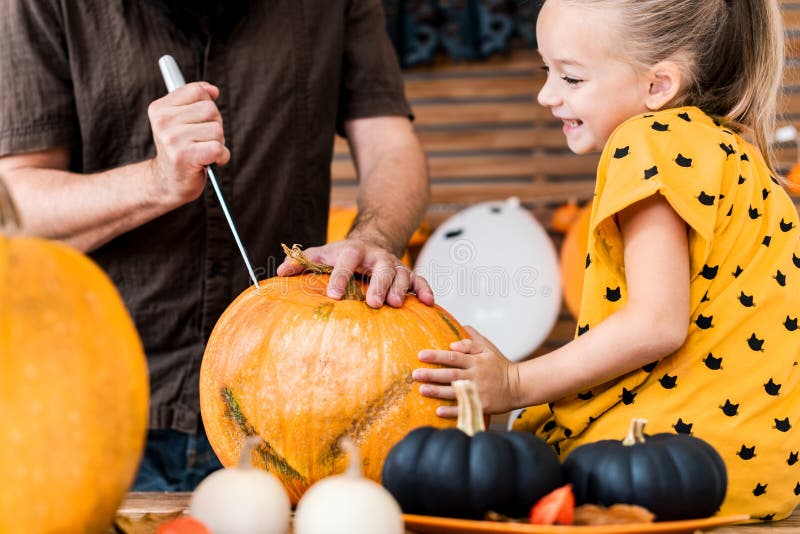 Jeune fille mignonne s'asseyant sur la table de cuisine, aidant son père à découper le grand potiron Mode de vie de famille de Ha photos libres de droits Jeune fille mignonne s'asseyant sur la table de cuisine, aidant son père à découper le grand potiron Mode de vie de famille de Ha photos libres de droits