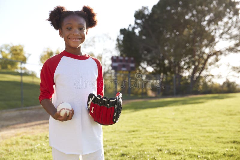Jeune fille noire tenant le base-ball et gant regardant à l'appareil-photo image stock Jeune fille noire tenant le base-ball et gant regardant à l'appareil-photo image stock