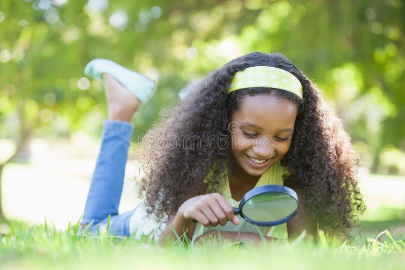 Jeune fille regardant l'herbe par la loupe en parc photo stock