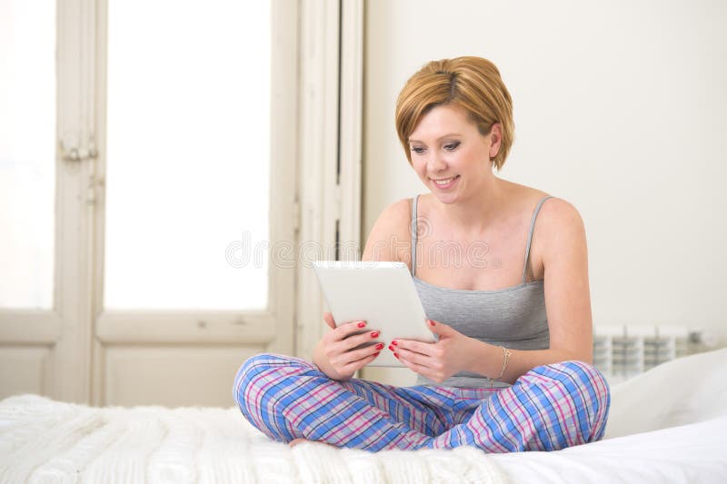 Jeune fille rouge attirante de cheveux dans le dessus de réservoir de sommeil et pantalon de pyjamas se reposant sur le lit à la photo libre de droits