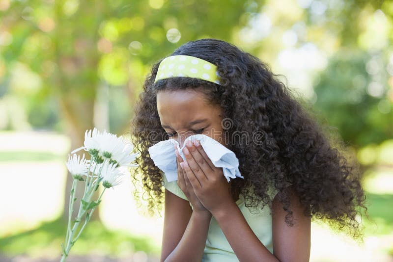 Jeune fille s'asseyant par la fleur et soufflant son nez en parc photographie stock