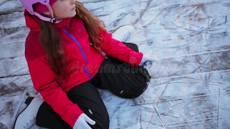 Jeune fille s'assoit à la glace dans des patins et des vêtements chauds clips vidéos