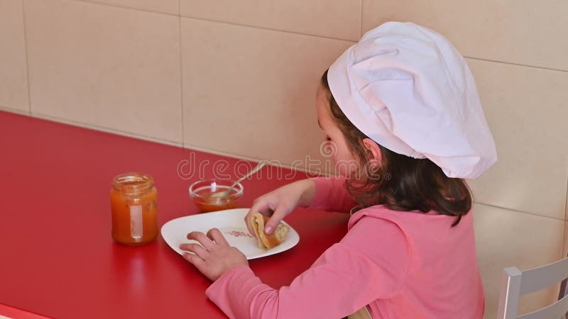 Jeune fille savoure un snack avec du pain grillé et de la confiture à une table rouge banque de vidéos