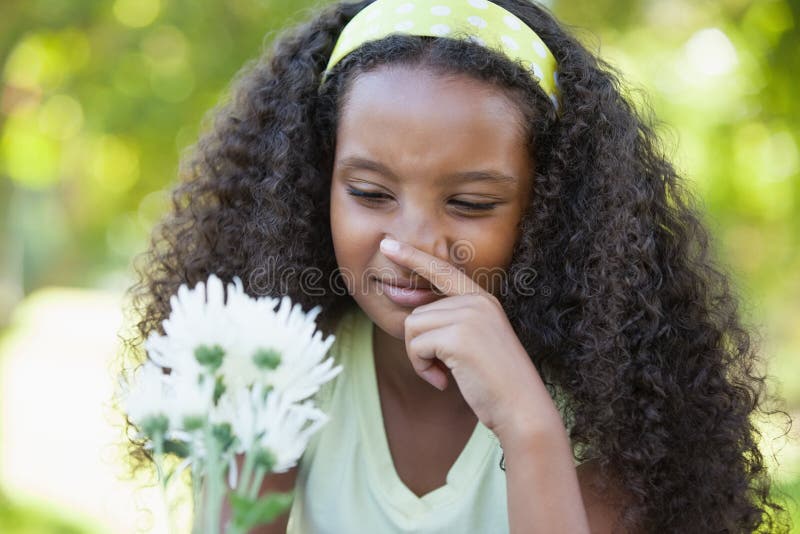 Jeune fille tenant une fleur et couvrant son nez en parc photographie stock