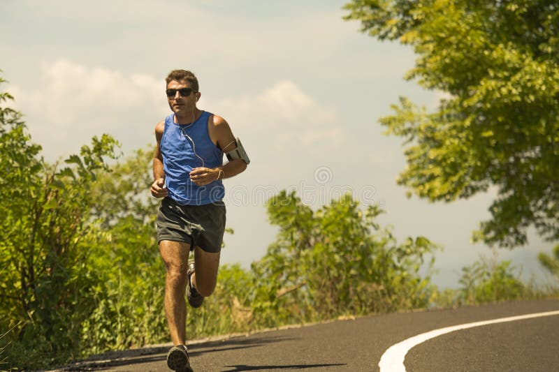 Jeune formation attrayante d'homme de coureur de sport dans la séance d'entraînement courante de route goudronnée par matin ensol photo stock Jeune formation attrayante d'homme de coureur de sport dans la séance d'entraînement courante de route goudronnée par matin ensol photo stock