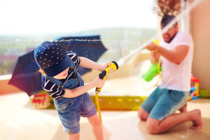 Jeune garçon enthousiaste ayant l'amusement, éclaboussant l'eau du père au jour d'été chaud photographie stock Jeune garçon enthousiaste ayant l'amusement, éclaboussant l'eau du père au jour d'été chaud photographie stock
