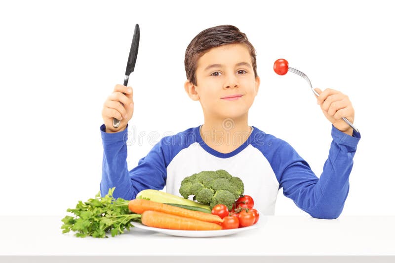 Jeune garçon mangeant des légumes posés à la table photos stock Jeune garçon mangeant des légumes posés à la table photos stock