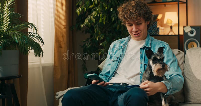 Jeune garçon souriant magasiner en ligne parle à son chien rires tient la carte de crédit à la main clips vidéos