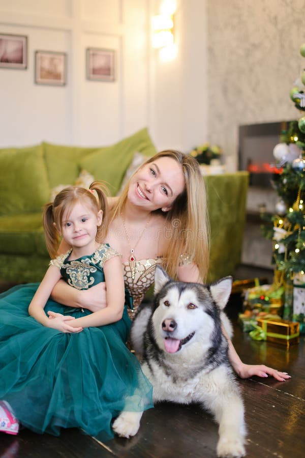 Jeune gentille mère avec la petite fille et le malamute se reposant près de l'arbre de Noël proche image libre de droits Jeune gentille mère avec la petite fille et le malamute se reposant près de l'arbre de Noël proche image libre de droits