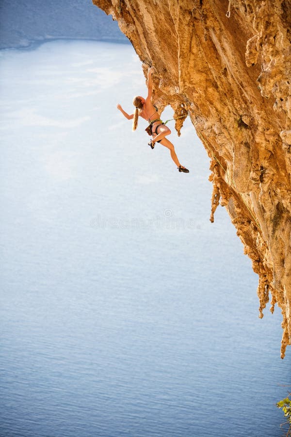 Jeune grimpeur de roche féminin dans le bikini accrochant avec une main sur la falaise image libre de droits Jeune grimpeur de roche féminin dans le bikini accrochant avec une main sur la falaise image libre de droits