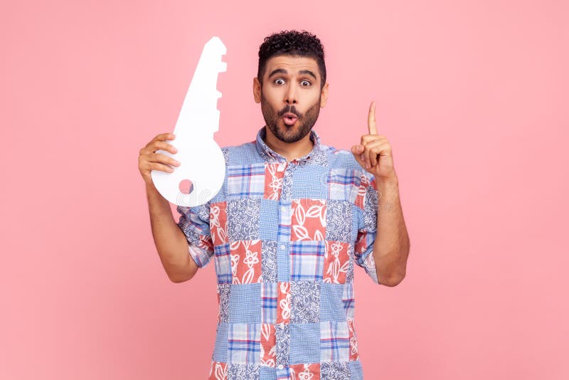 Jeune homme adulte avec barbe et cheveux foncés portant une chemise de style casual bleu tenant une grande clé en papier et pointa image libre de droits